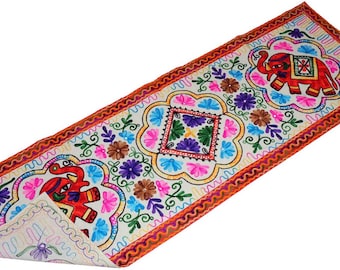 May include: A rectangular table runner featuring vibrant embroidery on a cream-colored fabric. The design includes two red elephants, floral motifs, and geometric patterns in shades of blue, purple, green, and orange, finished with a thick orange border.