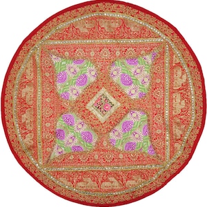 May include: A round, red decorative pillow with intricate gold embroidery and embellishments. The center features a square design with green and purple floral patterns. The pillow has a detailed border and a vibrant, eye-catching appearance.