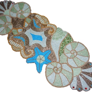 May include: A beaded table runner with a sea life design. The runner features various sea creatures, including starfish and seashells, in shades of blue, green, and brown. The design is embellished with small beads, creating a textured and decorative effect.