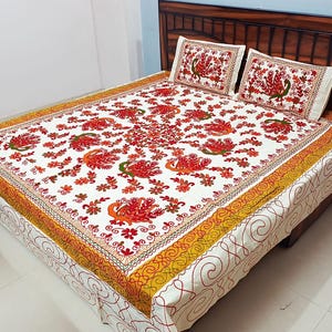 Peut inclure: Un couvre-lit blanc et deux taies d'oreiller assorties ornés de motifs de paons brodés en rouge et orange avec des touches de vert. La bordure présente un motif tourbillonnant jaune et orange, tandis que les côtés arborent un fin trait rouge.