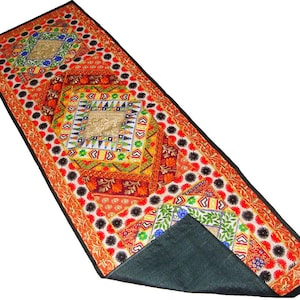 Könnte beinhalten: Ein rechteckiger Tischläufer mit einem lebendigen Patchwork-Design und aufwendigen Stickereien in Rot, Orange, Gelb, Grün und Blau. Das Muster umfasst geometrische Formen, florale Motive und einen schwarzen Rand, mit einer Rückseite aus dunkelgrauem Stoff.