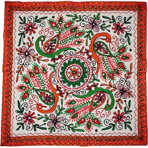 May include: A square textile featuring intricate embroidery with four stylised birds arranged around a central circular medallion. The design uses vibrant red, green, and orange thread on a white background, accented with small reflective mirrors.
