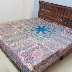 Peut inclure: Une couverture de lit avec un motif cachemire détaillé dans les tons de rose, de bleu et de vert. Le centre de la couverture de lit est de couleur turquoise vif. La couverture de lit est sur un cadre de lit en bois.