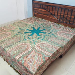 Puede incluir: Una cama con cabecero de madera y colcha estampada. La colcha presenta un diseño central turquesa rodeado de estampados de cachemira en tonos rojos, verdes y beige. La cama está contra una pared azul claro.
