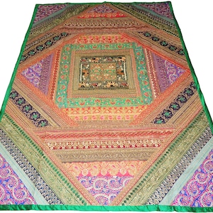 May include: A large, colorful textile with a patchwork design. The central square features intricate patterns in shades of green, orange, and brown. The surrounding sections display a variety of geometric shapes and patterns, with a green border. The textile is likely a decorative item.