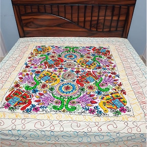 Peut inclure: Un couvre-lit blanc orné d'un panneau central avec des éléphants brodés colorés, des motifs floraux et des cercles en rouge, bleu, jaune, vert et violet. La bordure présente un motif continu de lignes sinueuses cousues à la main.