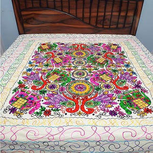 Peut inclure: Un couvre-lit couleur crème orné de broderies vives et multicolores représentant des éléphants, des paons et des motifs floraux. Le design comprend des motifs circulaires complexes et des lignes sinueuses en rose, vert, jaune et orange.