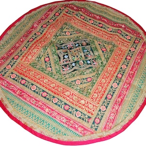 Könnte beinhalten: Runder, farbenfroher Textilartikel mit geometrischem Design. Die Mitte ist ein dunkelgrünes Quadrat mit floraler Stickerei. Das Design strahlt in Bändern aus Rot, Rosa, Grün und Gold aus, mit einem roten Rand. Wird wahrscheinlich als dekorativer Teppich oder Wandbehang verwendet, ca. 150 cm Durchmesser.