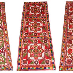May include: Three rectangular decorative textiles with detailed floral patterns. The textiles have a white background with red, green, and brown floral designs. The borders are decorated with colourful geometric patterns.