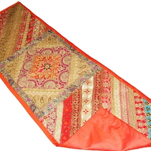 Op de afbeelding: Een rechthoekige tafelloper met een patchworkontwerp van rode, gouden en oranje stoffen panelen. De loper is versierd met ingewikkeld borduurwerk, accenten van metaaldraad en kleine reflecterende versieringen over het gehele oppervlak.