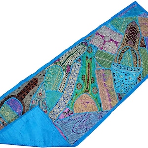 May include: A rectangular table runner featuring a vibrant patchwork of various fabrics in shades of blue, green, purple, and gold. The design includes intricate embroidery, metallic thread accents, and a solid bright blue border trim.