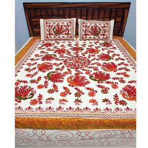 May include: White bedspread and two pillowcases with a vibrant embroidered design. The design features orange and red peacocks, flowers, and foliage. The bedspread has a yellow and orange border and is set on a wooden bed frame.