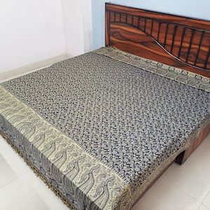 May include: A bedspread featuring a dark blue base with a dense, intricate gold paisley pattern throughout. The edges are finished with a wide, ornate gold border displaying a larger paisley motif and a decorative fringe along the bottom edge.