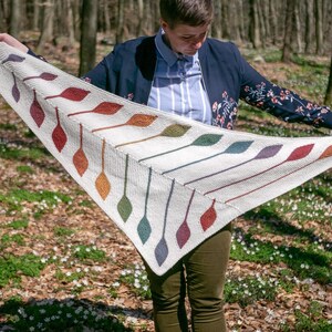 Op de afbeelding: Een witte driehoekige sjaal met een kleurrijk bladmotief. De sjaal is gemaakt van een getextureerd garen en heeft een franje rand.