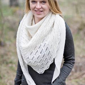 Może przedstawiać: Biały szal wykonany na szydełku z delikatnym wzorem koronkowym. Szal jest zarzucony na ramiona osoby w szarej koszuli z długim rękawem.