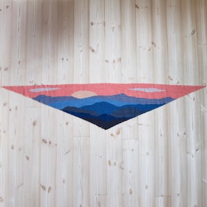 May include: A triangular wall hanging with a sunset scene over a mountain range. The sky is a light pink with a few clouds. The mountains are shades of blue and purple.