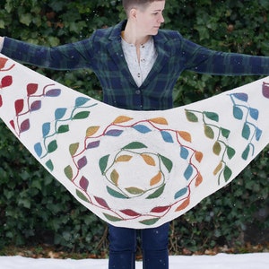 Könnte beinhalten: Ein weißer Häkel-Schal mit einem bunten Blätterdesign. Die Blätter sind in der Mitte des Schals kreisförmig und an den Rändern diagonal angeordnet.
