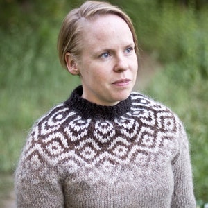 May include: A woman wearing a brown and white patterned sweater with a black collar. The sweater has a geometric design.