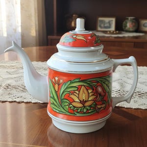 Puede incluir: Una tetera de porcelana blanca con una banda naranja vibrante alrededor del centro y la tapa. El cuerpo está decorado con un motivo floral colorido en tonos verdes, amarillos y marrones. La tetera incluye un pico curvo, un asa y una tapa.