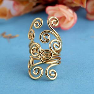 May include: A gold-coloured ring with a distinctive design of multiple swirls and curls. The ring appears to be made of a shiny metal and is set against a blue background. The ring's design is intricate and eye-catching.