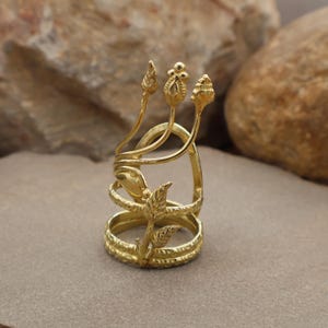 Könnte beinhalten: Ein goldfarbener Ring mit einem aufwendigen floralen Design. Der Ring hat drei vertikale, stilisierte Blütenknospen und mehrere Blätter. Der Ring hat ein gewickeltes Design mit mehreren Bändern und ist vor einem neutralen Hintergrund platziert.