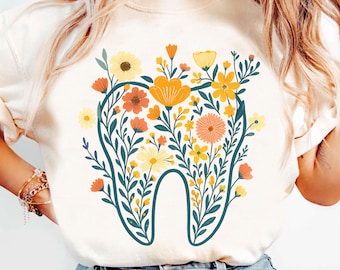 May include: Cream-colored sweatshirt featuring a floral tooth design. The tooth is outlined in teal and filled with yellow, orange, and peach flowers and green leaves. The design is centered on the front of the shirt.