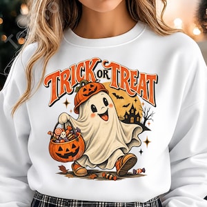 May include: A white long-sleeve sweatshirt featuring a graphic of a ghost wearing a pumpkin hat and carrying a jack-o'-lantern bucket filled with candy. The text TRICK OR TREAT is printed in orange above the ghost, with a haunted house silhouette.
