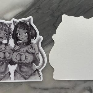 Puede incluir: Pegatina en blanco y negro con dos personajes femeninos de estilo anime con trajes de tem&aacute;tica felina. La pegatina tiene un borde blanco y una forma &uacute;nica. Los personajes sonr&iacute;en y llevan orejas de gato.