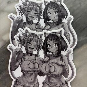 Puede incluir: Cuatro pegatinas en blanco y negro con ilustraciones de estilo anime de dos chicas con trajes de tem&aacute;tica felina. Cada chica tiene orejas de gato, un collar y una cola. Las pegatinas est&aacute;n sobre una superficie gris claro.