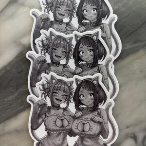 Puede incluir: Una pila de pegatinas en blanco y negro con dos personajes de estilo anime con disfraces de gato. Los personajes tienen orejas y colas de gato y est&aacute;n sonriendo. Las pegatinas est&aacute;n sobre un fondo blanco.