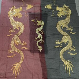 May include: Gold-colored dragon appliqués with intricate details, including scales and flowing forms, are displayed against red and black fabric. The dragons vary in size and design, showcasing a traditional Asian aesthetic.
