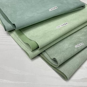 May include: Three folded pieces of suede fabric in varying shades of green. The top layer is labeled 57#冰荷绿, the middle layer is labeled 7102-1#浅果绿, and the bottom layer is labeled 59#蛋壳绿. Each piece features a soft, matte, textured surface.