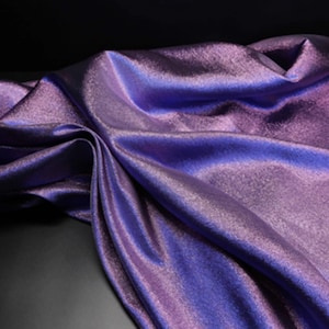 May include: A draped fabric with a shimmering, iridescent appearance. The material is a blend of purple and blue hues, creating a dynamic visual effect. The fabric's folds and curves add depth and texture to the image.