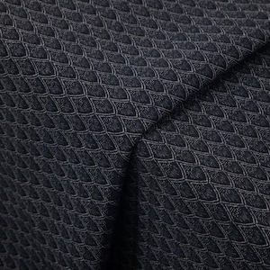 Op de afbeelding: Close-up van een donkerblauwe stof met een herhalend, getextureerd patroon. Het patroon bestaat uit kleine, onderling verbonden, schubachtige vormen in een lichtere, zilverachtige kleur, waardoor een subtiel contrast ontstaat. De stof is gevouwen en toont diepte en dimensie.