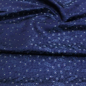 Könnte beinhalten: Ein tief dunkelblauer Stoff mit einem sich wiederholenden Muster aus kleinen weißen Sternen und stilisierten Wolkenmotiven. Das Textil hat einen subtilen Glanz und ein dichtes, komplexes Design mit geschichteten Texturen, die Tiefe erzeugen.
