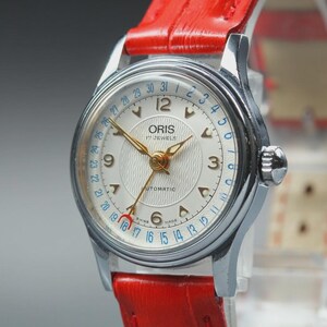 Puede incluir: Primer plano de un reloj automático Oris vintage con caja plateada y esfera blanca. El reloj presenta agujas e indicadores dorados, una pantalla de fecha y una correa de cuero roja. La esfera del reloj tiene el texto "ORIS 17 JEWELS AUTOMATIC".