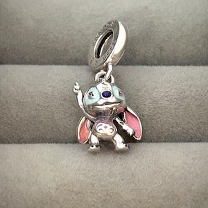 May include: A silver charm featuring a cartoon character with blue, pink, and purple enamel accents. The charm has a loop at the top for attaching to a bracelet or necklace. The character has large ears and is in a standing pose.