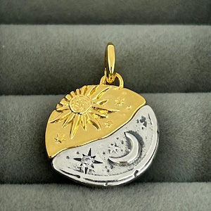 Pode incluir: Pingente bicolor em ouro e prata com design de sol e lua. A metade superior é dourada com um sol, a metade inferior prateada com uma lua crescente, estrelas e um diamante. O pingente tem uma argola dourada.