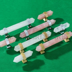 May include: A collection of crystal cabinet pulls in various colors, including pink and white. The pulls have a rectangular shape with metal accents and are set against a green background. The hardware is designed for furniture and home decor.