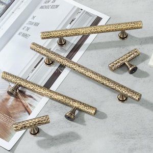 Puede incluir: Un conjunto de tiradores y manijas de gabinete de latón antiguo. El herraje presenta un diseño texturizado y martillado con un acabado cálido y envejecido. Los tiradores son de varios tamaños y formas, adecuados para cajones y puertas.