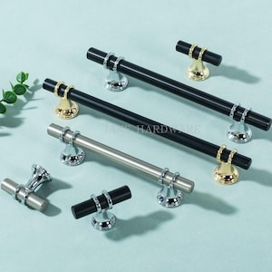 May include: An assortment of cabinet hardware, including black and silver bar pulls and matching knobs. The pulls have silver or gold accents and are displayed on a light blue surface. The text "JANT HARDWARE" is visible.