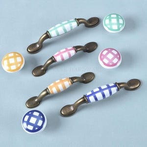 May include: A selection of cabinet handles and knobs. The handles have a bronze finish with ceramic centres in green, pink, orange, and blue plaid patterns. Matching knobs are also included.