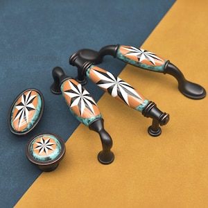 May include: Cabinet hardware set with a starburst design. The handles and knobs have a black base with a turquoise and orange starburst pattern. The hardware is displayed on a blue and gold background.