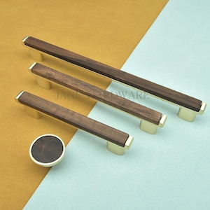 May include: A set of cabinet hardware featuring a dark wood grain center with gold-toned metal accents. The set includes three rectangular handles of varying lengths and a round knob. The hardware is displayed on a two-tone background of gold and blue.