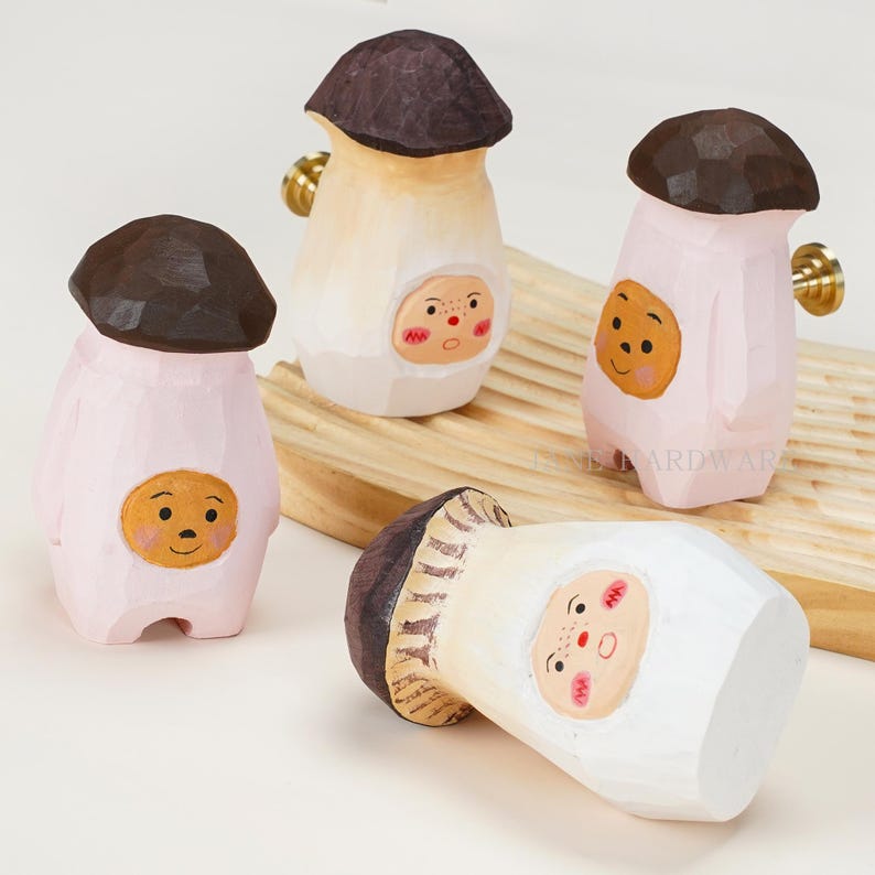 Op de afbeelding: Vier gesneden houten knoppen in de vorm van paddenstoelen met donkerbruine hoeden en lichtgekleurde stelen. Elke steel heeft een geschilderd gezicht met roze wangen. Twee knoppen hebben messingkleurige bevestigingen aan de zijkant.