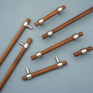 May include: A collection of wooden cabinet pulls with a brushed nickel finish. The pulls have a cylindrical wooden body with a metal ring and a small, protruding handle. The wood is a warm brown color, and the metal is silver.