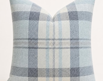 May include: A square throw pillow featuring a woven plaid pattern in shades of light blue, white, and dark grey. The fabric has a visible textured weave, and the design consists of intersecting horizontal and vertical stripes forming a classic grid.