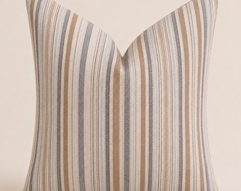 May include: A square throw pillow featuring a vertical striped pattern in shades of tan, light brown, grey, and off-white. The fabric has a visible woven texture with alternating thin and thick stripes running from the top to the bottom edge.