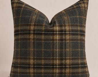May include: A square throw pillow featuring a dark charcoal gray and brown plaid pattern. The fabric displays a woven texture with intersecting horizontal and vertical lines in shades of tan and white, creating a classic grid design across the surface.