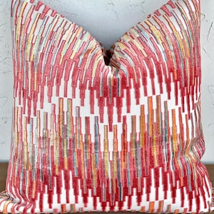 May include: A red, white, and yellow geometric patterned throw pillow with a white background. The pillow has a rectangular shape and is made of a soft, textured fabric.